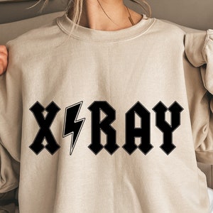 May include: A beige sweatshirt with a black graphic print that says "X-RAY" in a stylized font with a lightning bolt.
