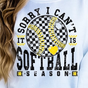 May include: White sweatshirt with a black and yellow graphic that says "Sorry I can't it's softball season". The graphic features a checkered softball with a yellow heart.