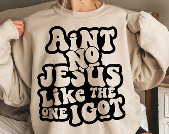 May include: A beige sweatshirt with a black graphic print that reads "Ain't No Jesus Like The One I Got".