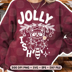 May include: A maroon crewneck sweatshirt featuring a white graphic of a raccoon hanging from a pine branch decorated with ornaments and string lights. The text JOLLY ISH is printed in large white letters above and beside the raccoon illustration.