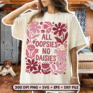 May include: Cream-colored t-shirt with a floral design in shades of pink and burgundy. The text "ALL OOPSIES NO DAISIES" is centered within the floral arrangement. The bottom of the image includes text: "300 DPI PNG + SVG + EPS + DXF FILE".