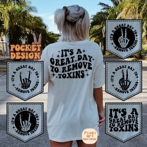 May include: A white t-shirt with a black graphic that says "It's a great day to remove toxins". The graphic features a skeleton hand making a rock and roll hand gesture. The t-shirt has a pocket on the front with a similar graphic.