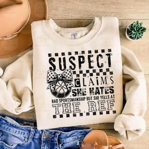 May include: A white sweatshirt with a black graphic print that says "SUSPECT CLAIM'S SHE HATES BAD SPORTSMANSHIP BUT SHE YELLS AT THE REF".