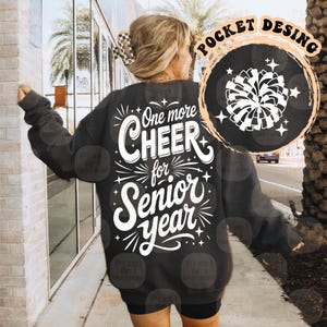 May include: Dark gray sweatshirt with the text "One more CHEER for Senior year" in white. A circular graphic with a white pom-pom and stars is on the upper right. The sweatshirt is a casual style.