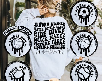 Op de afbeelding: Een wit sweatshirt met zwarte tekst die "Uniform Washer, Water Bottle Filler, Ride Giver, Snack Maker, Picture Taker, Sideline Cheerleader, #SportsMom" luidt. Er zijn vijf zwarte en witte cirkels met verschillende sportpictogrammen en de tekst "Sports Mom" rond elk pictogram.