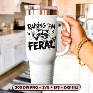 K&ouml;nnte beinhalten: Ein wei&szlig;er Becher mit einer schwarz-wei&szlig;en Grafik eines Waschb&auml;ren mit dem Text "Raising 'em Feral".