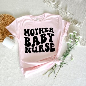 K&ouml;nnte beinhalten: Rosa T-Shirt mit schwarzem Text, der in einer Retro-Schrift "Mother Baby Nurse" lautet.