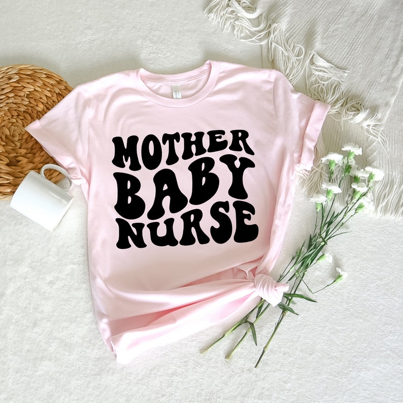 K&ouml;nnte beinhalten: Rosa T-Shirt mit schwarzem Text, der in einer Retro-Schrift "Mother Baby Nurse" lautet.