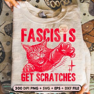May include: A light beige sweatshirt with the red text "FASCISTS GET SCRATCHES" and a red illustration of an angry cat. The design includes a cross and the text "300 DPI PNG + SVG + EPS + DXF FILE".