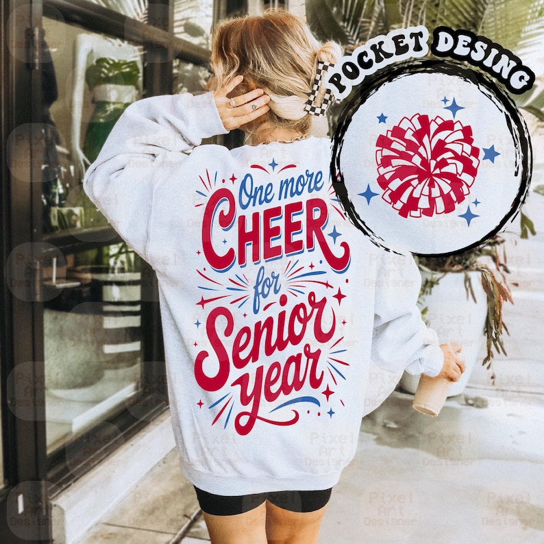 May include: A light gray sweatshirt with the text "One more CHEER for Senior Year" in red and blue. A circular design on the upper right features a red and white pom-pom with blue stars. The sweatshirt has a crew neck and long sleeves.