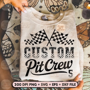 Op de afbeelding: Een beige sweatshirt met een racethema. Het ontwerp toont twee gekruiste geblokte vlaggen boven de woorden "CUSTOM Pit Crew" in een vetgedrukte letter, met het nummer "5" eronder. De sweatshirt is opgevouwen.