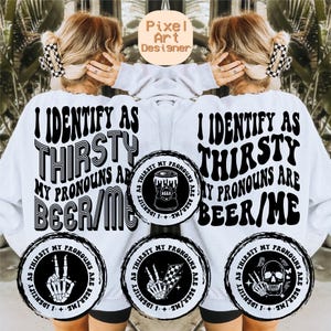 Può includere: Felpa bianca con la scritta nera "I IDENTIFY AS THIRSTY, MY PRONOUNS ARE BEER/ME". Il design include grafiche circolari con illustrazioni di birra e mani di scheletro. Il logo Pixel Art Designer è in alto.