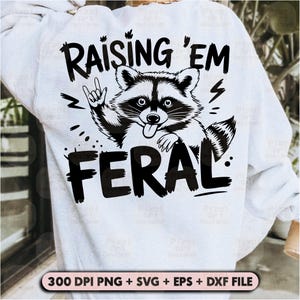 K&ouml;nnte beinhalten: Ein wei&szlig;er Pullover mit einer schwarzen Grafik eines Waschb&auml;ren mit dem Text "Raising 'em Feral".