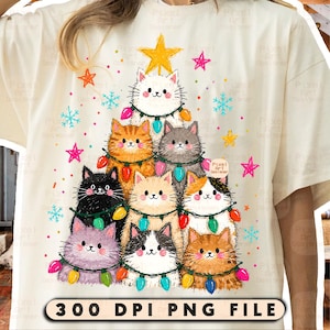 May include: A cream-colored t-shirt featuring a graphic of nine cats arranged in a triangular Christmas tree shape, decorated with colorful string lights, yellow stars, and blue snowflakes. The text 300 DPI PNG FILE is at the bottom.