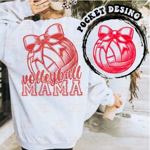 Może przedstawiać: Biała bluza z czerwonym nadrukiem piłki siatkowej i tekstem "volleyball mama" nadrukowanym na plecach. Piłka siatkowa ma czerwoną kokardkę.
