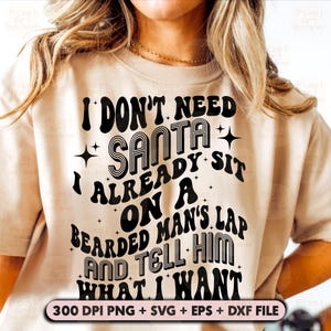 Könnte beinhalten: Ein beiges T-Shirt mit einer schwarzen Grafik, auf der steht "Ich brauche keinen Weihnachtsmann, ich sitze schon auf dem Schoß eines bärtigen Mannes und sage ihm, was ich will". Die Grafik ist im Retro-Stil mit fetten, umrandeten Buchstaben gehalten.
