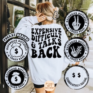 May include: A white sweatshirt with the text "Expensive Difficult & Talks Back" in black, retro-style lettering. The sweatshirt has four black and white circular designs with the same text and different graphics, including a money bag, a skeleton hand, and a checkered flag.