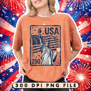 Może przedstawiać: Pomarańczowa koszulka z grafiką przedstawiającą Statuę Wolności, amerykańską flagę i napis "USA". Grafika jest w kolorach niebieskim i białym. Numer "250" znajduje się pod pomnikiem. Koszulka ma kr&oacute;tkie rękawy.