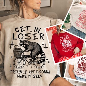 Può includere: Una felpa beige con un'illustrazione in bianco e nero di un procione che guida una bicicletta. Il testo "Get in Loser" è scritto in rosso sopra l'illustrazione e "Trouble ain't gonna make it self" è scritto in rosso sotto l'illustrazione.