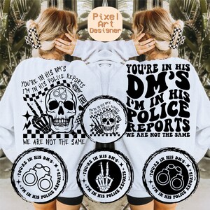 Puede incluir: Sudadera blanca con un estampado gráfico negro que dice "You're in his DM's I'm in his police reports We are not the same". El gráfico incluye una calavera con esposas, un signo de paz y un patrón a cuadros.