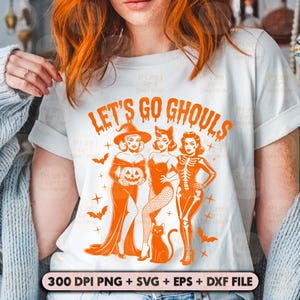 May include: White t-shirt with an orange graphic that reads "LET'S GO GHOULS." The graphic features three women in Halloween costumes, bats, and a black cat. The bottom of the shirt has the text "300 DPI PNG + SVG + EPS + DXF FILE."