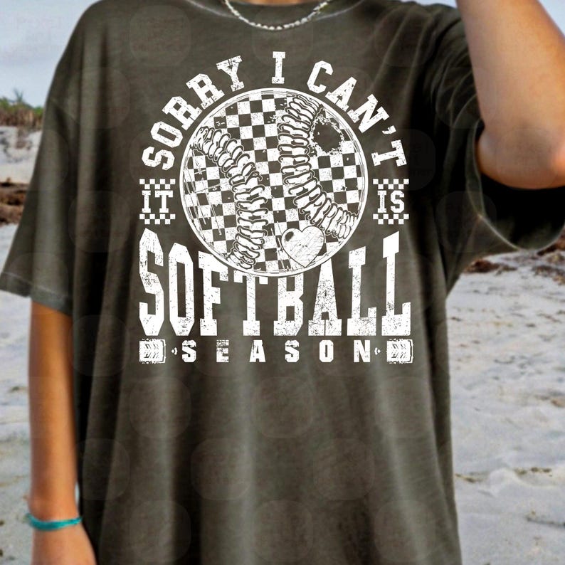May include: A green t-shirt with a white graphic that says "Sorry I can't it is softball season". The graphic features a softball with a checkered pattern and a heart.