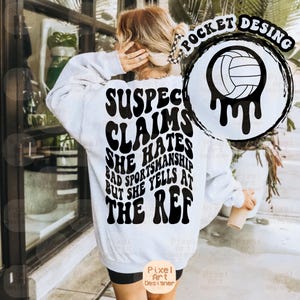 Könnte beinhalten: Ein weißes Sweatshirt mit schwarzem Text auf dem Rücken. Der Text lautet "SUSPECT CLAIMS SHE HATES BAD SPORTSMANSHIP BUT SHE YELLS AT THE REF." Auf der rechten Seite befindet sich eine schwarz-weiße Volleyballgrafik. Das Sweatshirt hat lange Ärmel.