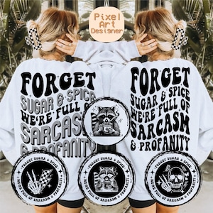 May include: White sweatshirt with black text that reads "Forget Sugar & Spice We're Full of Sarcasm & Profanity". The text is in a retro font. There are three smaller circles with black and white illustrations of a raccoon, a skeleton hand, and a skull.