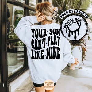 Peut inclure: Sweat-shirt blanc avec un texte noir qui dit "Your son can't play like mine" dans une police rétro. Un graphique noir et blanc d'un ballon de football avec de la peinture qui coule se trouve dans le coin supérieur droit. Le texte "Pocket Desing Football Mom" est autour du graphique du ballon de football.