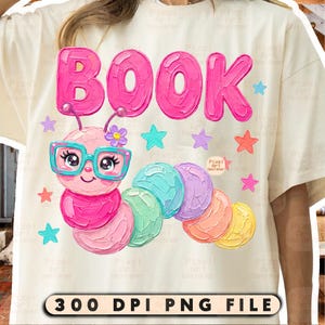 May include: A cream-colored t-shirt featuring a graphic of a pink caterpillar wearing teal glasses with the word BOOK in pink letters above it. The design includes small colorful stars and a flower. The bottom text reads 300 DPI PNG FILE.