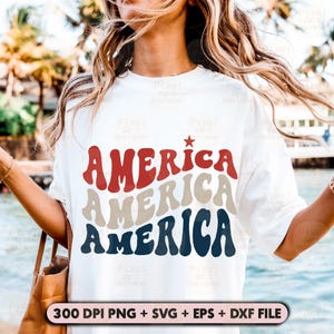 May include: A white t-shirt with the word "AMERICA" written three times in a retro font. The word is stacked on top of itself, with each layer in a different color: red, beige, and blue. A small red star is above the top layer of the word.