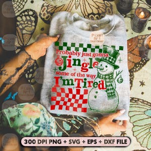 May include: A light gray sweatshirt with a Christmas-themed graphic. The design features a snowman wearing a top hat and scarf, along with the text "Probably just gonna Jingle some of the way I'm Tired" in red and green.