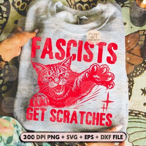 May include: A gray sweatshirt with the words "FASCISTS GET SCRATCHES" in red, along with a red illustration of a cat. The sweatshirt also includes the text "300 DPI PNG + SVG + EPS + DXF FILE".