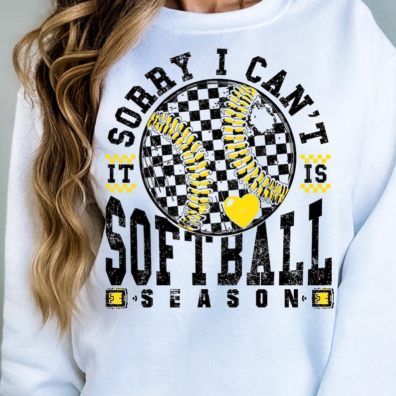 May include: White sweatshirt with a black and yellow graphic that says "Sorry I can't it's softball season". The graphic features a checkered softball with a yellow heart.