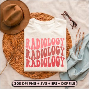May include: A white t-shirt with the word "RADIOLOGY" repeated three times in a retro font. The text is in shades of pink and red. The t-shirt is lying on a woven straw mat with a brown hat and glasses nearby.