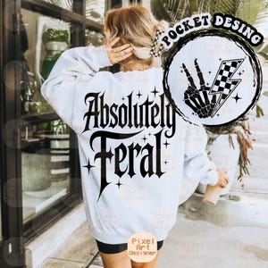 May include: White sweatshirt with black text that reads "Absolutely Feral" and a black and white graphic of a skeleton hand giving the peace sign with a lightning bolt and chequered pattern.