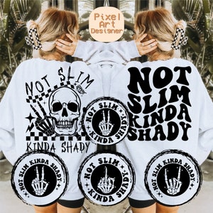 以下が含まれることがあります： 黒い文字で「Not Slim Kinda Shady」と書いてある白いスウェットシャツと、骸骨のグラフィック。テキストはレトロなフォントスタイル。同じテキストと骨格の手のグラフィックが描かれた小さな円が3つある。