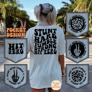 Puede incluir: Una camiseta blanca con el texto "STUNT HARD TUMBLE STRONG HIT ZERO" en negro. La camiseta tiene un bolsillo en la parte delantera con el texto "HIT ZERO" en negro. Hay cuatro parches en blanco y negro con el texto "STUNT HARD TUMBLE STRONG HIT ZERO" y diferentes gráficos.