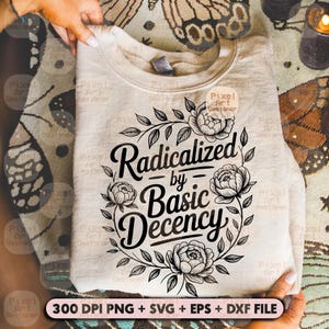 May include: A light beige sweatshirt featuring the text "Radicalized by Basic Decency" within a black floral wreath. The sweatshirt is folded and held by hands. The bottom of the image includes text: "300 DPI PNG + SVG + EPS + DXF FILE."