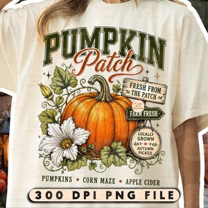 Puede incluir: Una camiseta color crema con un gráfico de una calabaza naranja grande con hojas verdes y una flor blanca. El texto dice PUMPKIN PATCH, FRESH FROM THE PATCH, FARM FRESH, LOCALLY GROWN AUTUMN PICKED, PUMPKINS, CORN MAZE, APPLE CIDER, 300 DPI PNG FILE.