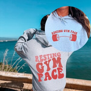 May include: A gray hoodie with the text "Resting Gym Face" in red letters on the back. The front of the hoodie has a smaller version of the text with a red barbell graphic.