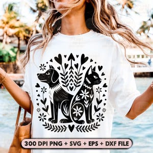 May include: White t-shirt featuring a black and white graphic of a dog and cat surrounded by floral and heart designs. The text "300 DPI PNG + SVG + EPS + DXF FILE" is at the bottom. The shirt is being worn by a person.