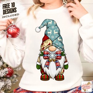 Könnte beinhalten: Weißes Sweatshirt mit einem Weihnachtszwerg-Design. Der Zwerg hat eine blaue Mütze mit Rentier- und Schneeflockenmustern, einen weißen Bart und eine rot-blaue Schleife. Der Text "FREE 10 DESIGNS INCLUDED" befindet sich oben links.