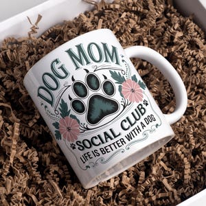 May include: White ceramic mug with a floral design and the text "Dog Mom Social Club Life is Better with a Dog".