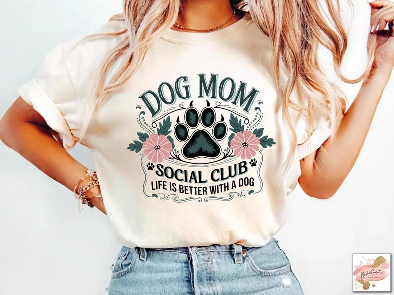 May include: A white t-shirt with a vintage-style graphic that says "Dog Mom Social Club Life is Better with a Dog". The graphic features a black paw print with pink flowers.