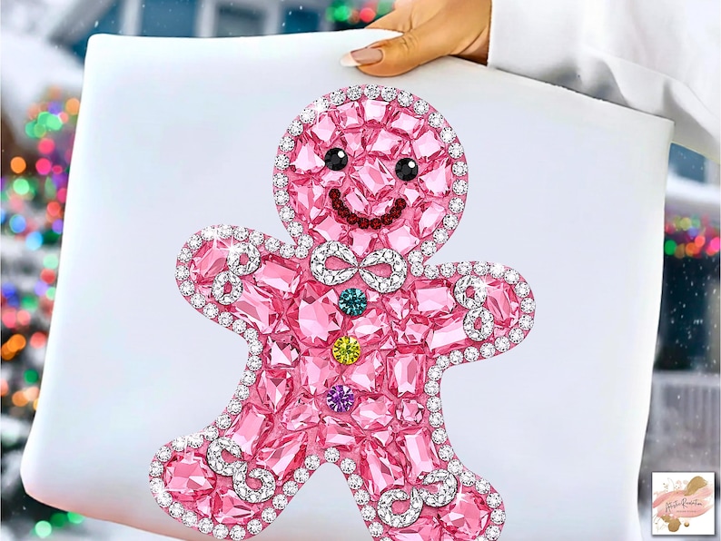 Puede incluir: Un dise&ntilde;o de hombre de jengibre rosa con una apariencia brillante y similar a una gema. La figura tiene una cara sonriente, una pajarita y est&aacute; delineada con cristales transparentes. El dise&ntilde;o se establece sobre un fondo blanco, lo que sugiere un tema navide&ntilde;o.