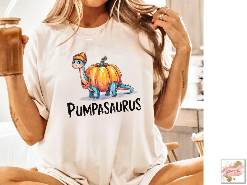 May include: A white t-shirt with a cartoon dinosaur wearing a pumpkin as a hat. The text "Pumpasaurus" is printed below the dinosaur.