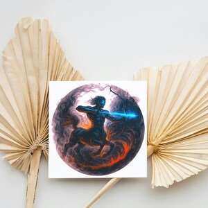 May include: A square print featuring a centaur archer with a glowing blue arrow, set against a dark, swirling background with orange and purple hues. The artwork is placed in front of dried palm leaves.