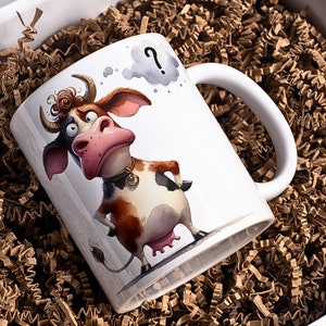May include: White ceramic mug featuring a cartoon cow with a confused expression and a thought bubble with a question mark. The cow has brown and white markings, a pink nose, and a gold collar. The mug is presented in a white gift box with brown paper filler.