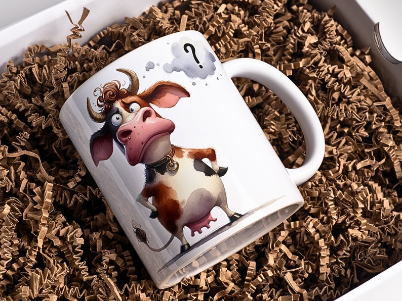 May include: White ceramic mug featuring a cartoon cow with a confused expression and a thought bubble with a question mark. The cow has brown and white markings, a pink nose, and a gold collar. The mug is presented in a white gift box with brown paper filler.